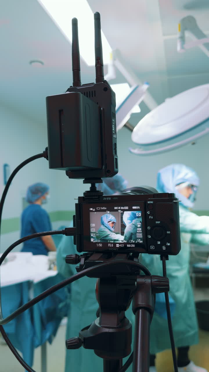 Kyiv, Ukraine, 2 August 2025: Vertical close-up of a digital camera recording a surgery with a wireless video transmitter. The foreground focus is on the advanced setup, capturing the working surgeons in the background