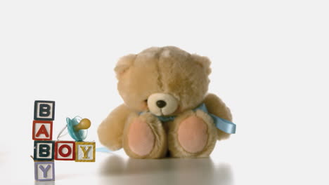 teddy bear falling besides baby blocks and blue soother