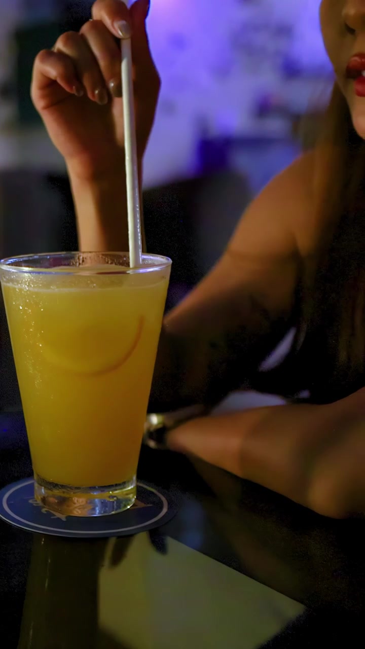Primo piano di una mano che mescola un cocktail giallo con una cannuccia di notte, con luci bokeh, in un lounge moderno.
