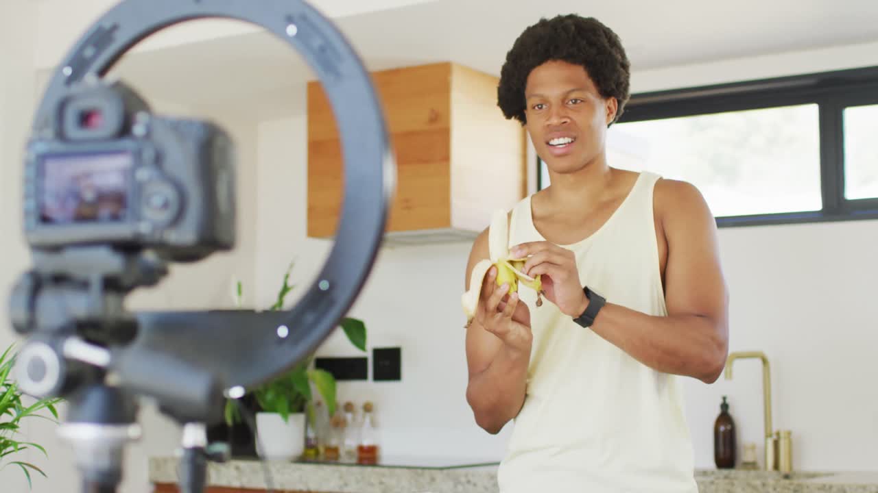 Uomo afroamericano in forma cucina, prepara un frullato e filma un vlog.