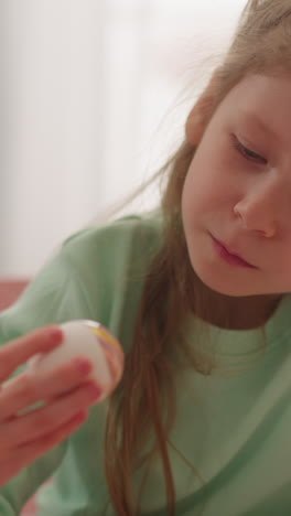 thoughtful little girl holds easter egg colored with marbling patterns in room closeup slow motion. creative ideas for spring holiday decorations