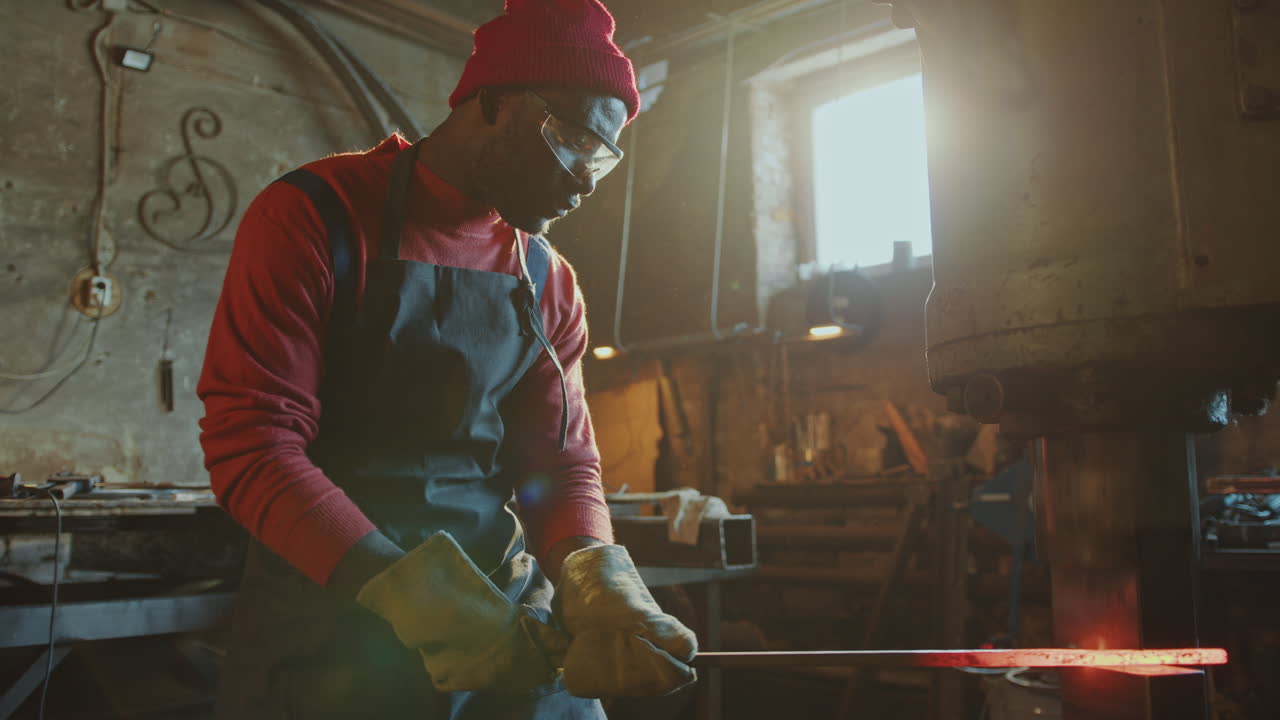 African American Blacksmith Forging Iron Billet with Press Machine in Workshop
