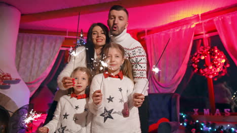 new year celebration at home. portrait of young family at christmas on fireplace background. happy parents and their kids with sparkling lights.