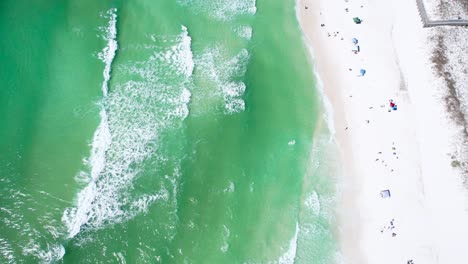 aerial view of waves in clear emerald waters and a white sand beach on a sunny day