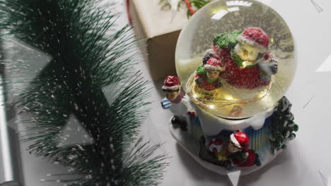 animation of snow falling over christmas snow globe and decorations