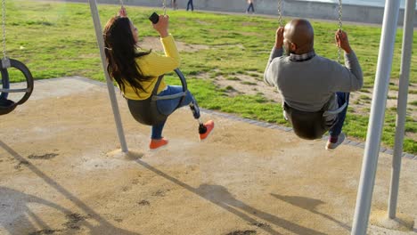 Rear-view-of-couple-playing-on-playground-swing-in-the-park-4k