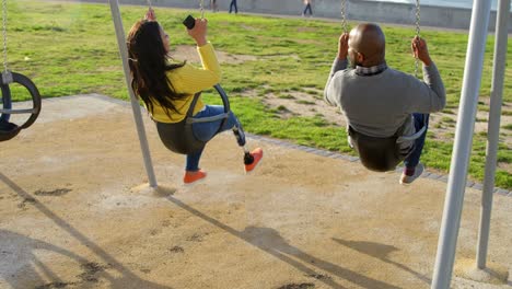 rear view of couple playing on playground swing in the park 4k