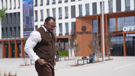 african guy walking at urban street. african american business man answering phone call outdoors. smiling afro male talking on smartphone outside.