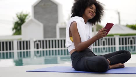 a female dressed for exercise sits on a yoga mat talking smart phone video call.