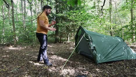 male traveler successfully finishes setting up a tent at the campsite in the woods-1