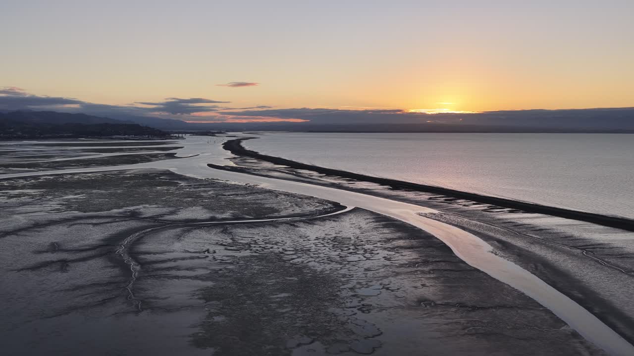 Flyfoto av svingete tidevannselv som møter kystlinjen ved solnedgang i New Zealand, filmatiske introer, naturbakgrunner og kystlandskapsutsikt