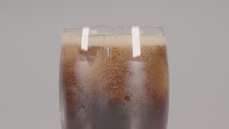 cubitos de hielo cayendo en un vaso de cola y la superficie de la bebida hace espuma, sobre un fondo blanco de estudio
