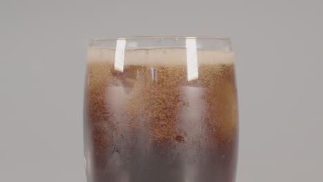 ice cubes dropping into glass of cola and the surface of the drink foams - against a white studio background