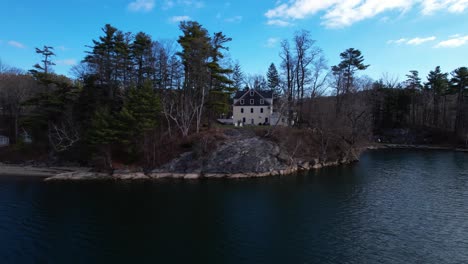 evergreen trees and colonial home on a lakeside with blue skies and rolling hills in the background