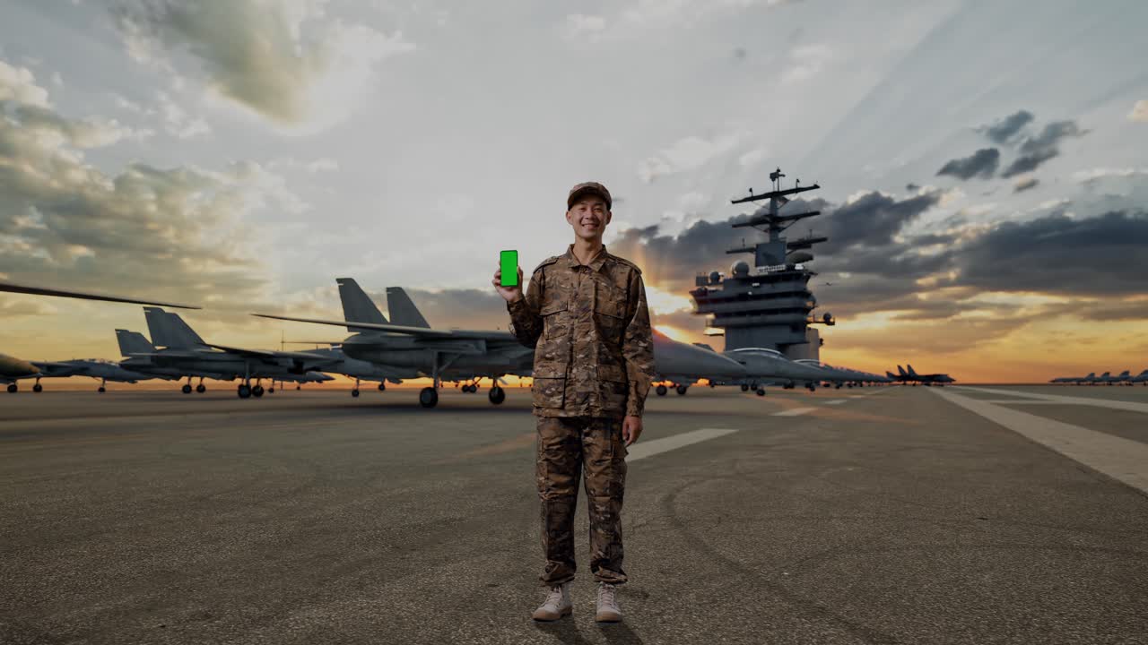Full Body Of Asian Man Soldier Smiling And Showing Green Screen Smartphone To The Camera While Standing On Aircraft Carrier