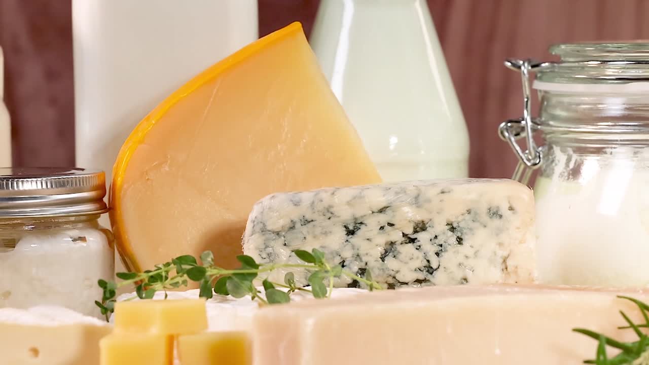 Close-up of assorted cheeses and milk bottles on a wooden surface with herbs.