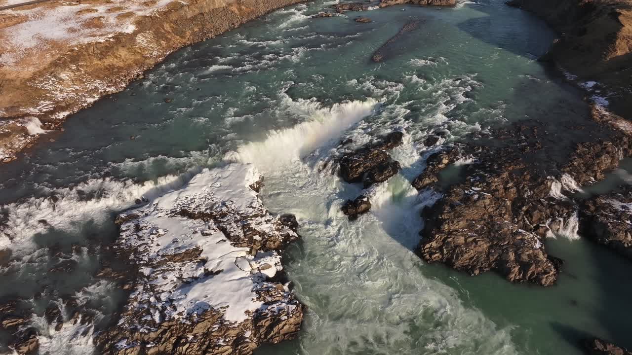 Top-down aerial view of the magnificent Urriðafoss waterfall in Iceland, showcasing its massive water flow cutting through snowy terrain.