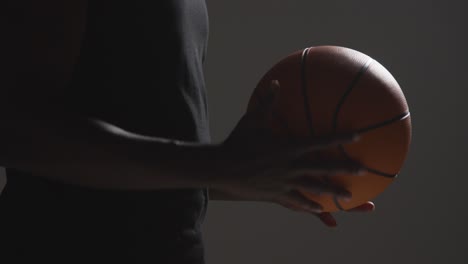 close up studio shot of male basketball player throwing ball from hand to hand against dark background