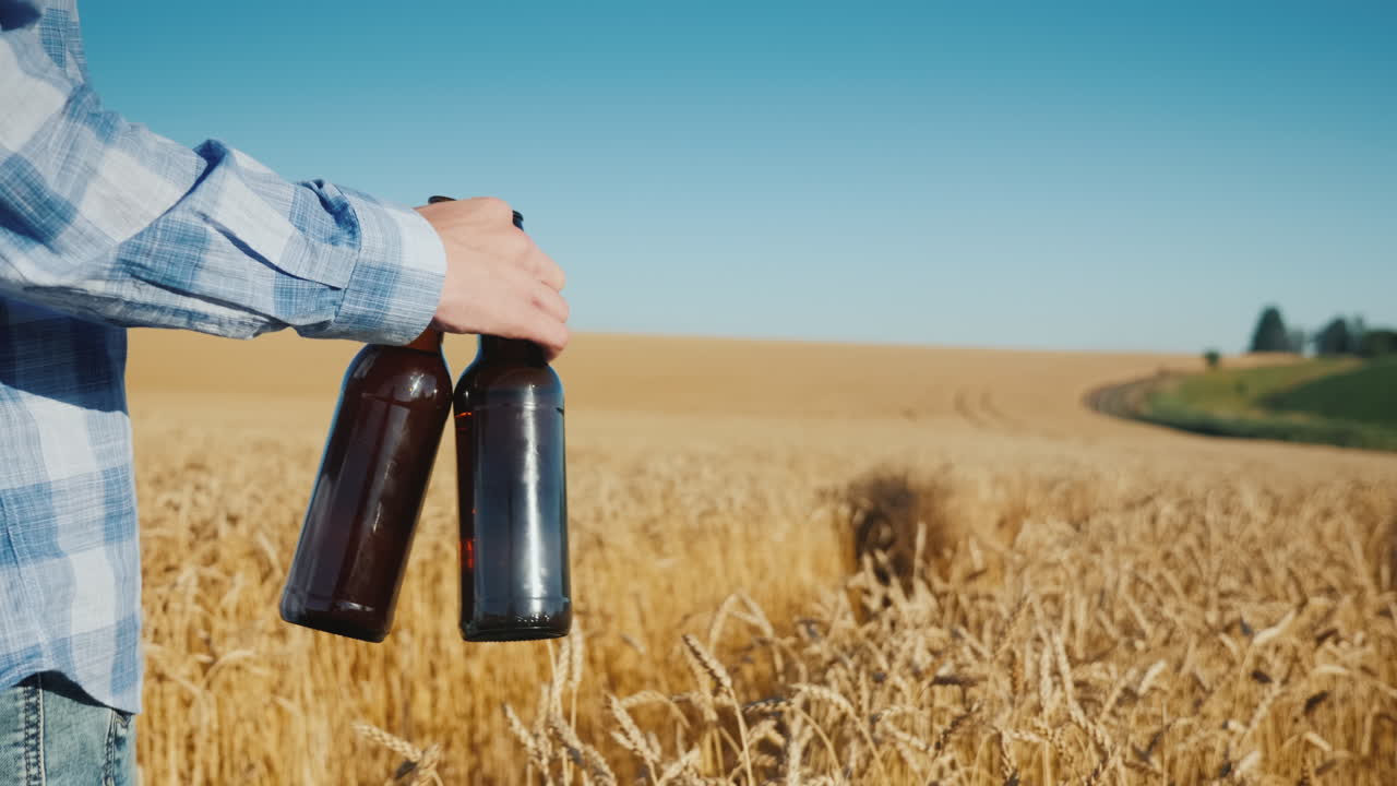 granjero camina por un campo de trigo lleva dos botellas de cerveza en la mano