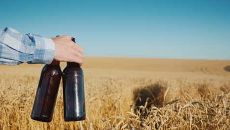 granjero camina por un campo de trigo lleva dos botellas de cerveza en la mano