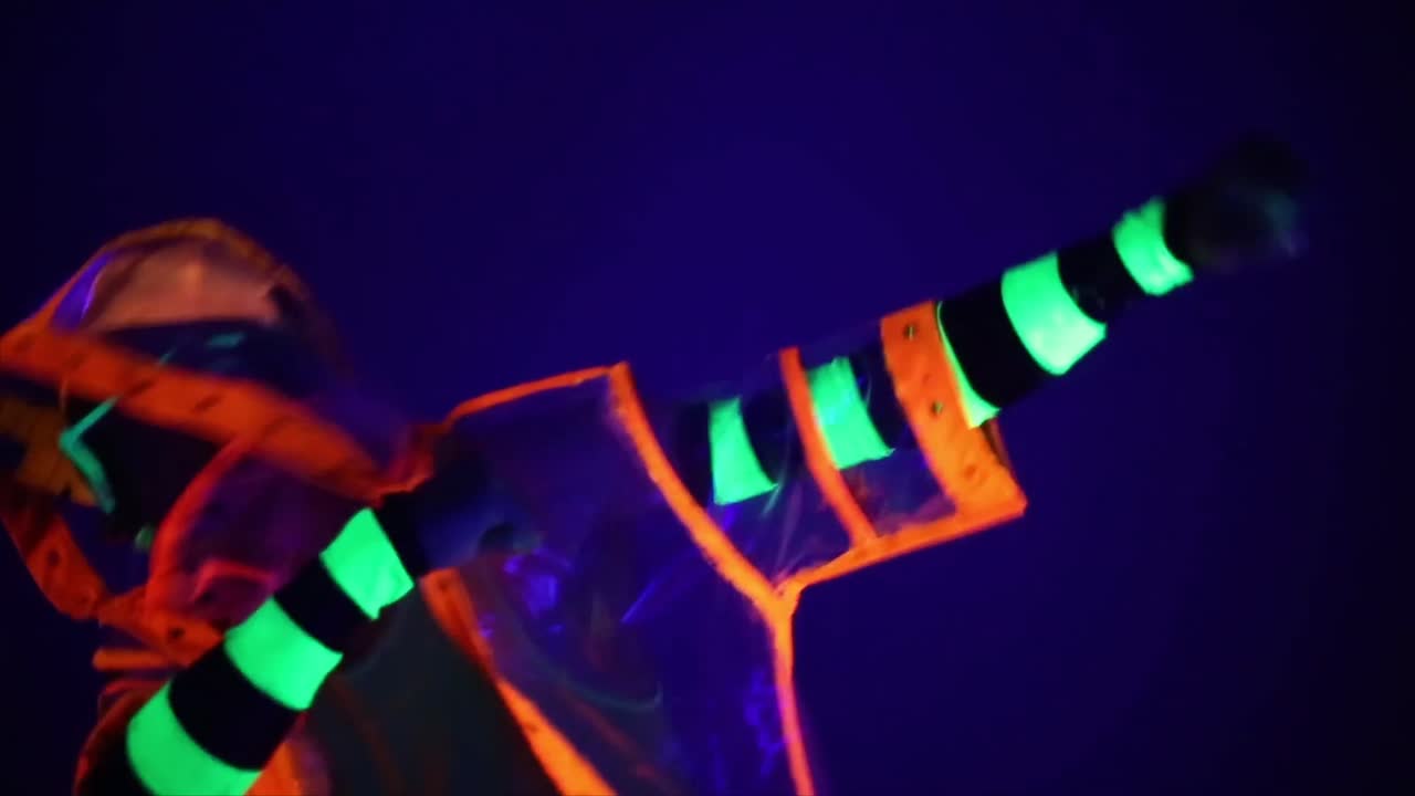 Person danser i neon-lysende outfit under sortlys