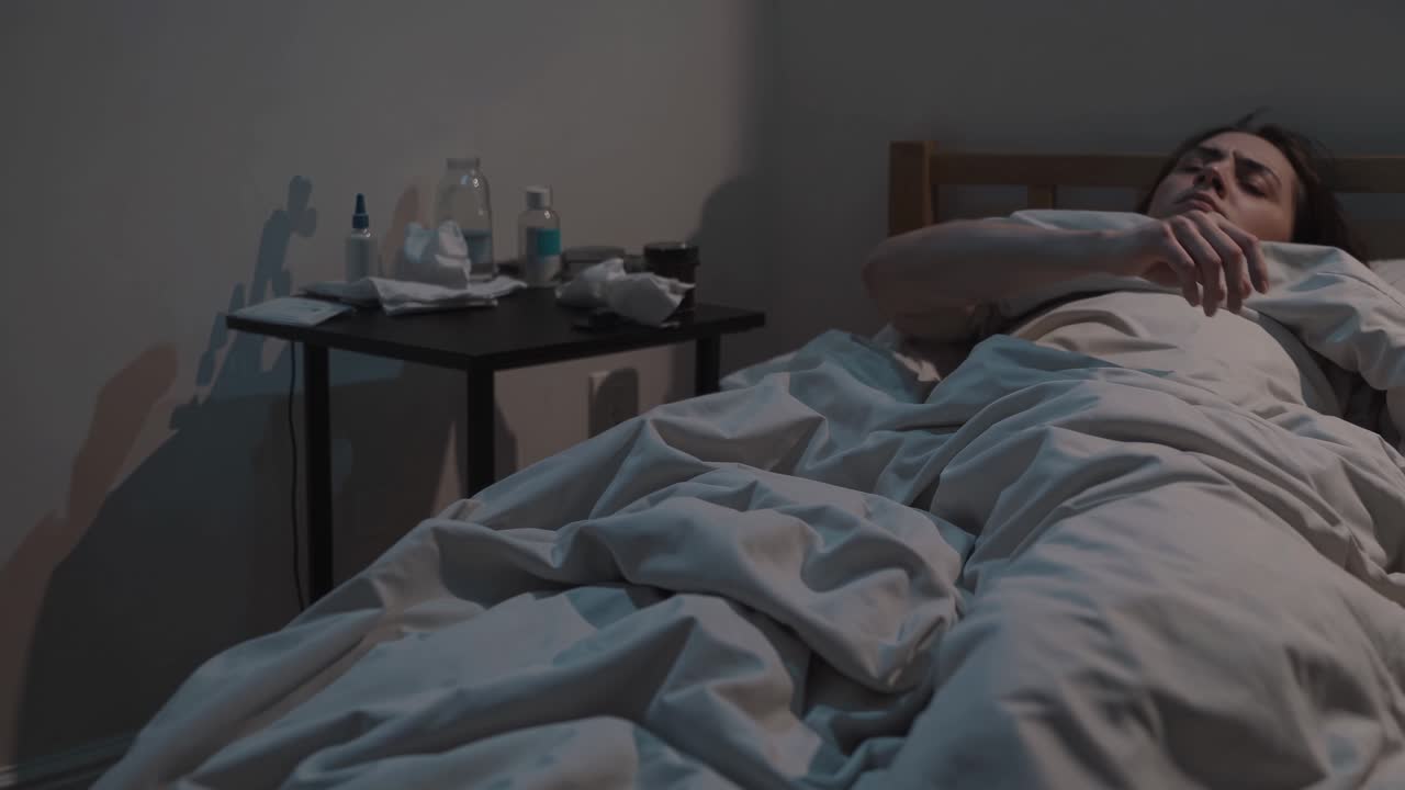 Una scena video malinconica cattura una persona a letto da un'angolazione laterale, evidenziando un'atmosfera di solitudine.