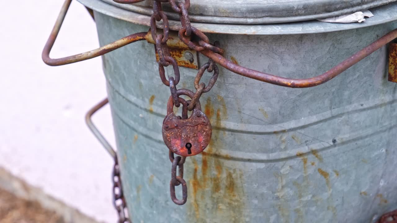 금속 쓰레기통은 에 불법 쓰레기를 버리는 것을 막기 위해 녹슬은 잠금과 사슬로 고정되어 있습니다.