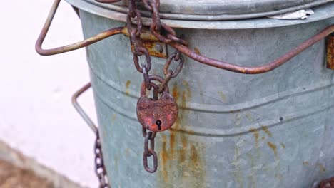 contenedor de basura metálico asegurado con cerrojo y cadena oxidados para evitar el vertido ilegal en el vecindario de cerca