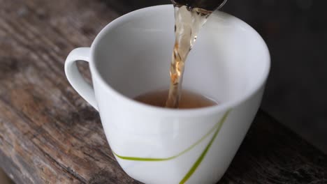 toma en cámara lenta de verter una taza de té en una taza blanca sobre una mesa de madera