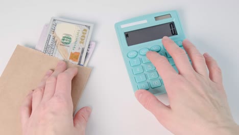 male hand counts expenses or income on a calculator as well as cash in dollars.