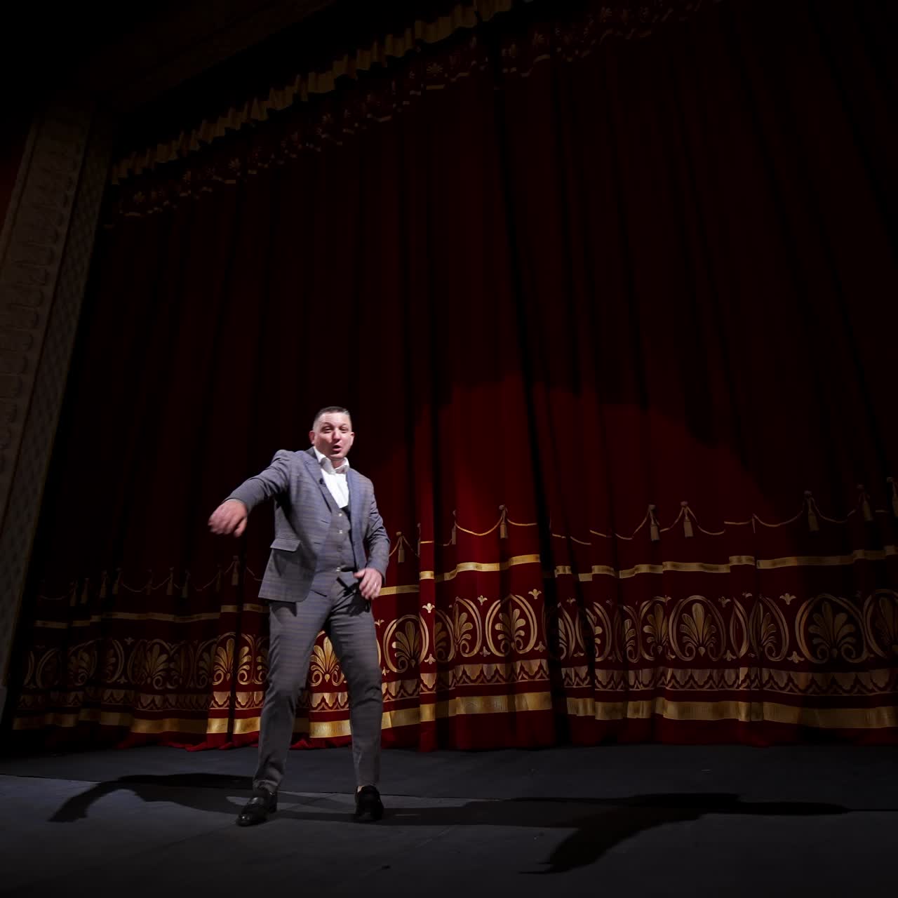 Actor in suit on large theater stage. Male comedian telling jokes and dancing gestures on the scene. Joyful performer on stage