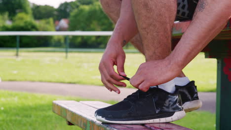 male runner sitting on bench tying shoelaces, low section