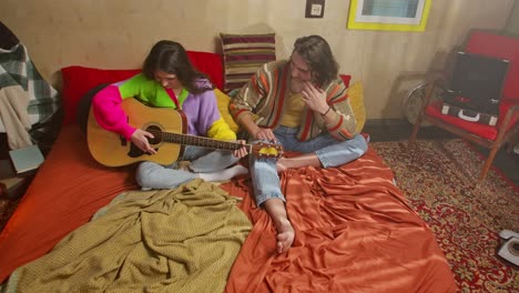 couple playing acoustic guitar in a cozy retro bedroom