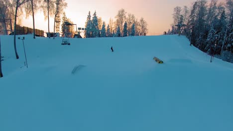 Forward-moving-aerial-view-of-a-passing-snowboarder-in-a-terrain-park-at-sunset