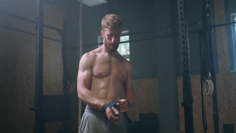 young athletic caucasian man changing putting weight lifting straps on in gym locker room before workout slow motion. ties arms to barbell with fitness straps.