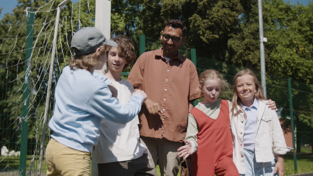 A diverse group of children and an adult man on a sunny sports field