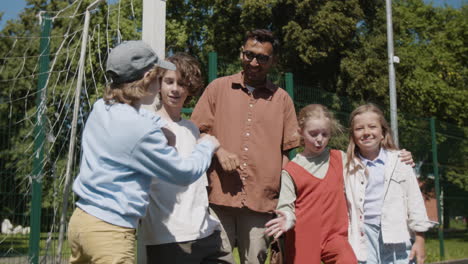 a diverse group of children and an adult man on a sunny sports field