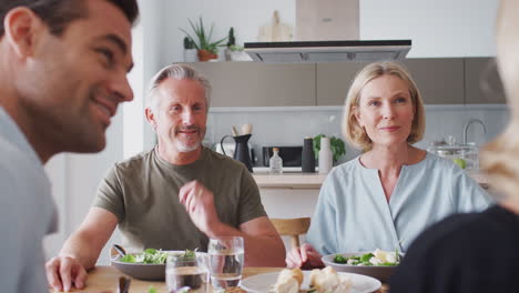 family with senior parents and adult offspring eating meal around table at home together