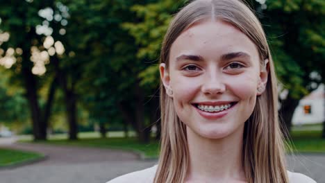 joven alegre con aparatos ortopédicos de pie con confianza entre la exuberante vegetación del parque, irradiando energía positiva y felicidad genuina en un entorno natural sereno