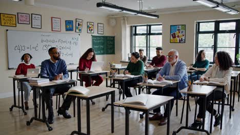 Adult students and a young boy are attentively taking notes during a lesson in a bright, modern classroom, showcasing a diverse group engaged in education
