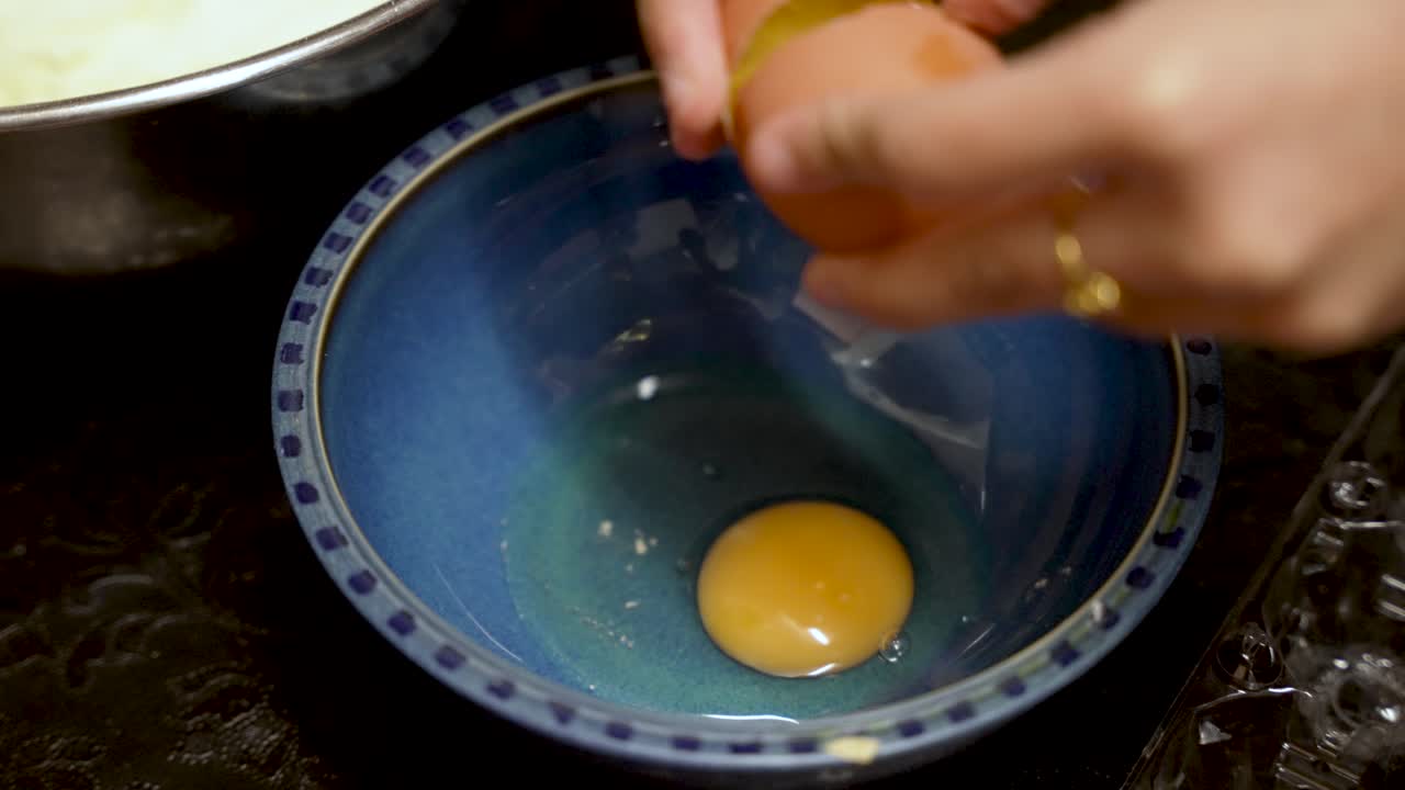 Close-up of hands cracking an egg into a blue bowl, preparing for a recipe.