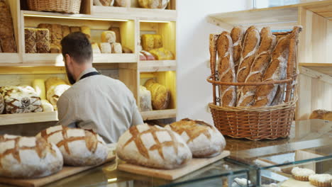 Der-Männliche-Verkäufer-In-Der-Bäckerei,-Der-Gerade-Gebackenes-Brot-Zur-Theke-Bringt