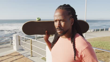 Video-of-african-american-man-holding-skateboard-by-sea