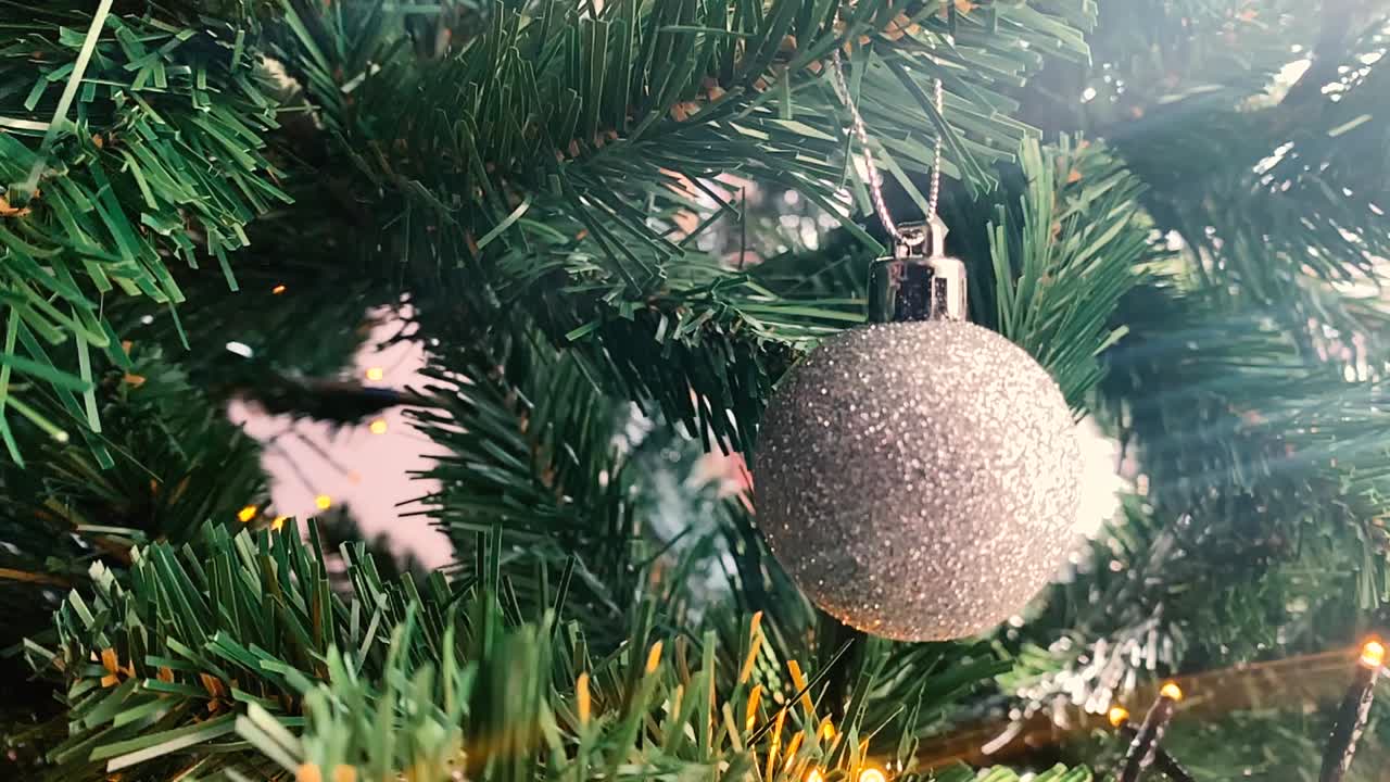 Slowmotion of swinging Christmas bulb. Bouncing silver ball Christmas decorations on a Christmas tree in slow motion. Round Christmas bulb decorations on spruce branch tree.