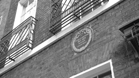 monochrome shot of plaque commemorating novelist charles dickens on the exterior brick wall of charles dickens museum in london, uk