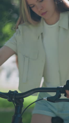 primer plano de una mujer agarrando el manillar de una bicicleta negra, usando guantes de motociclista, el fondo presenta vegetación exuberante con hojas que se mueven suavemente en la brisa