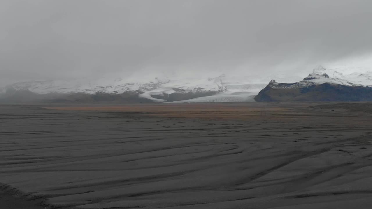 Aerial panning shot of mountains behind a black sand beach in Iceland
