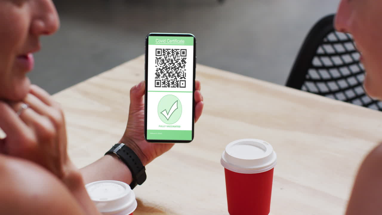 Man at cafe showing smartphone with covid vaccination certificate and qr code on screen