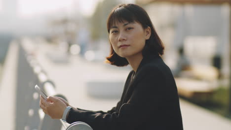 portrait of asian businesswoman with smartphone on embankment