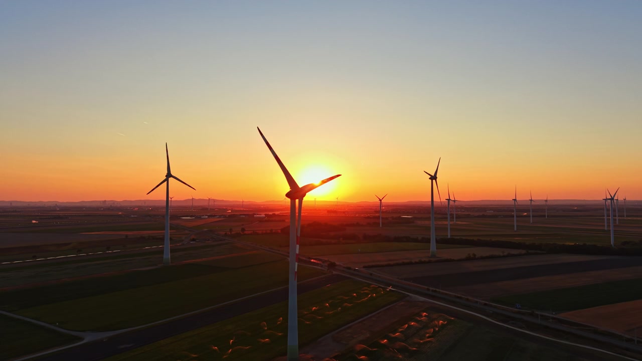 Wind turbines are turning as the sun sets behind them in a wide open field
